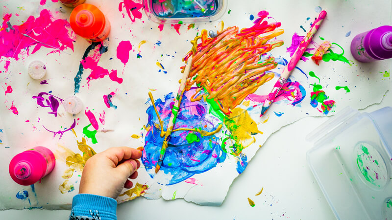 child's hands painting with bright colors